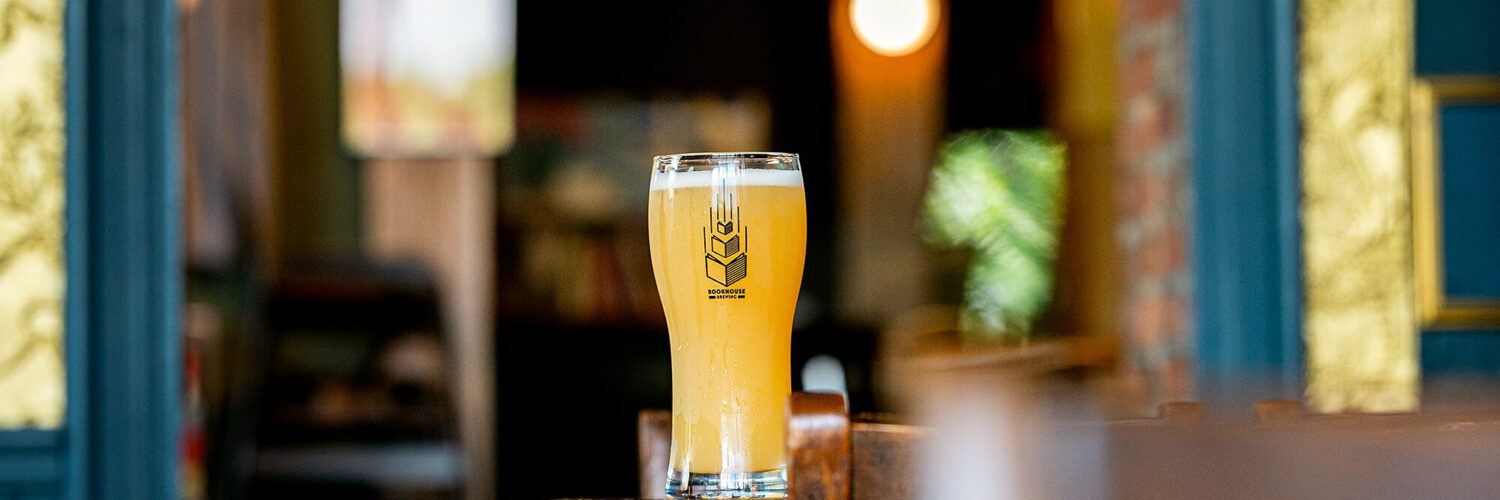 A filled pint glass bearing the Bookhouse Brewing logo, sitting on a bar