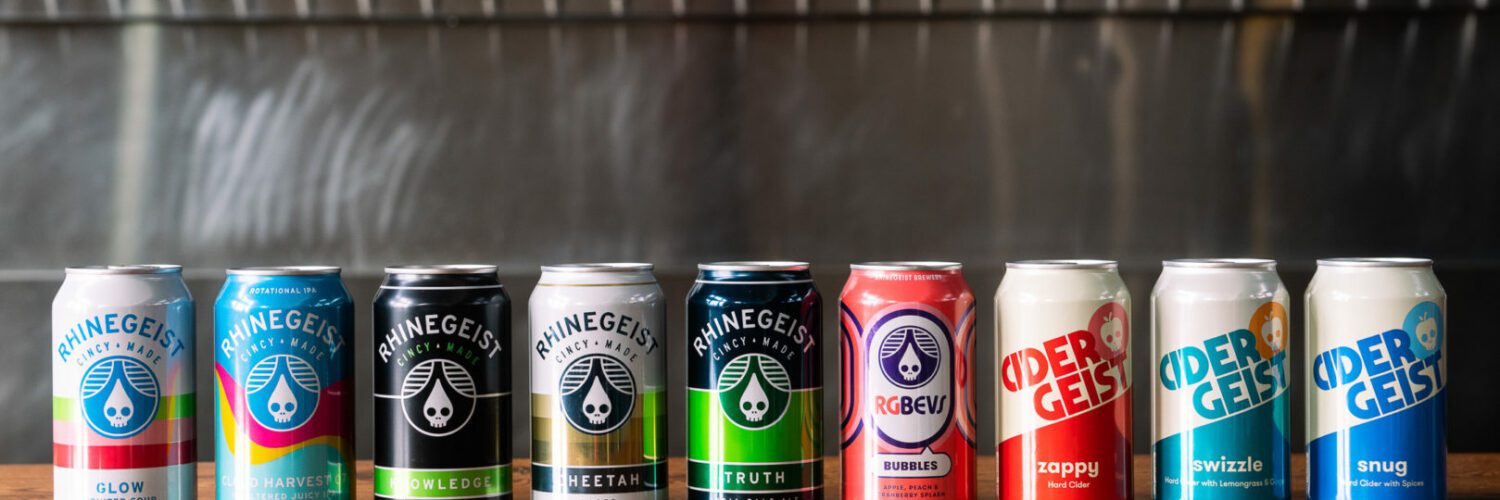 A color line of Rhinegeist beer cans in a line on a wooden bar, with a row of taps in the background