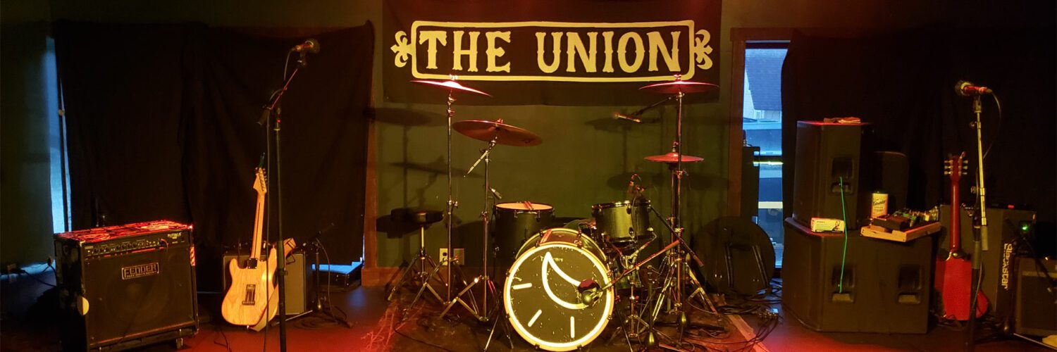 The stage of The Union, with red floors, a drum set, a guitar, and other equipment